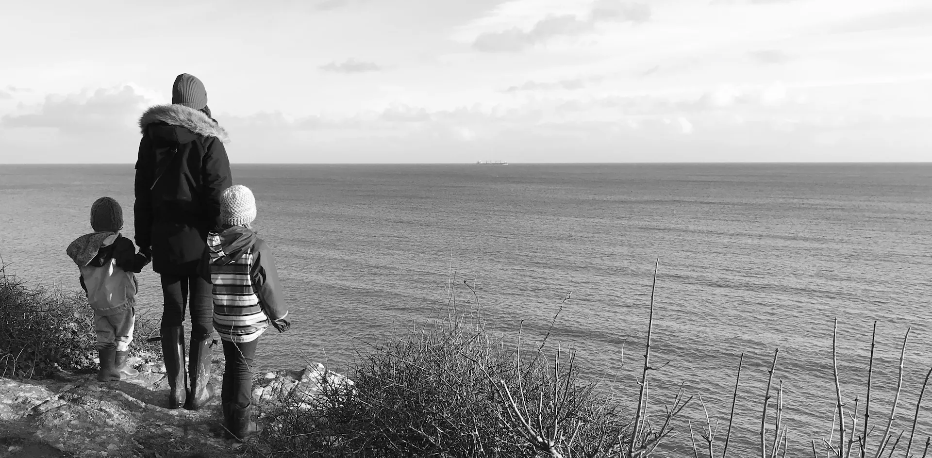 Reflexologist mum standing with children on a cliff top in Cornwall looking out to sea